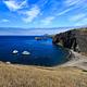 Harbor with boats, kayaks, and visitors on the beach. Steep island cliffs and other islands in the distance. 