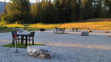 Gravel campsite area with multiple fire pits, picnic tables, and hoses visible — useful closeup of campsite amenities and surface treatment on the property.