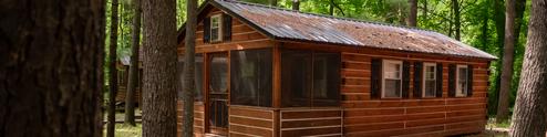 Exterior photo of a screened wooden cabin among trees (page header for Cabins) — clearly shows the property’s cabin accommodations and wooded setting.