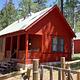 A sunny day illuminates Patterson Guard Station. The bright red color of the Guard Station contrasts the green conifer trees behind it. 