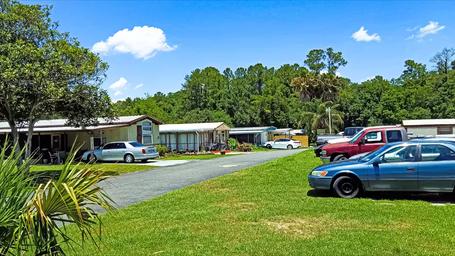 Street-level image of mobile homes and parked vehicles with landscaped lawns and trees — highlights residential units and onsite vehicle parking typical for the park (from the official site).