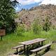 Campsite with bear box, picnic table, and fire ring. Trees and mountains in background