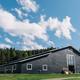 Wide exterior shot of the large black barn/event building on the property with grassy foreground and treeline — clearly depicts the main facility and setting.