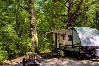 Well-lit campsite scene with travel trailer, picnic table and fire ring — good close view of a campsite setup and facilities (tables, level pad). Image is on the campground page.