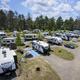 Aerial/drone-style shot of multiple RVs and pull-through sites with trees and roads visible — clear depiction of the RV campground layout and site density.