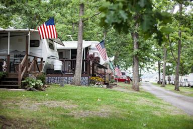 Row of RV sites with decks and American flags along a tree-lined drive — good depiction of site spacing, decks and mature trees on the property (IMG_0660.jpg from the camping page).