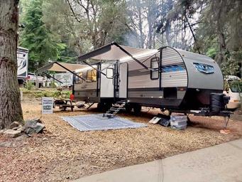 Large travel trailer at a developed campsite with mat, picnic and road — useful close view of an RV setup and site amenities on the property.