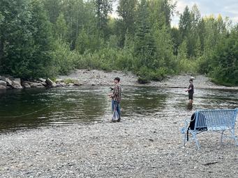 Riverside scene showing anglers standing in the creek and a bench on the shore — illustrates waterfront access and fishing activity available at the campground (from main site imagery and fishing-related pages).