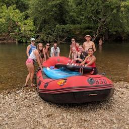 River activity shot showing a raft and group on the riverbank — represents the campground’s canoe/raft rentals and river recreation offerings shown on the site.
