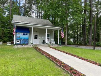 Small gray building with porch, ice machine, walkway, and American flags in a grassy area.
