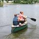 Two people canoeing on a lake with shoreline and RVs visible in the distance — depicts canoeing activity and the campground’s lake recreation (from site gallery/feature images).