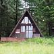 Brown A-Frame Cabin with steps leading up to it and trees behind and beside it. Berg Bay Cabin