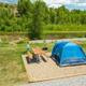 Tent site on a defined gravel pad with picnic table and river/vegetation in background — useful scenic campsite view showing tent pitches and nearby water; included in the campground’s gallery.