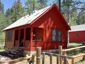 A sunny day illuminates Patterson Guard Station. The bright red color of the Guard Station contrasts the green conifer trees behind it. 