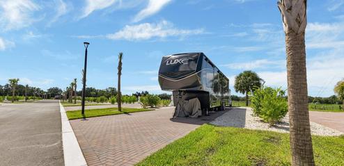 Paved RV pad with a fifth-wheel parked, landscaping and palm trees—useful depiction of an individual RV site and shown on the Plan Your Stay/gallery pages.