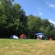 Open grassy tent field with multiple tents and tree line — shows tent camping area and site layout (Tent page).