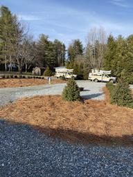 Labeled 'Site-8' image showing gravel RV sites, small trees, and park maintenance vehicles — direct photo of site layout and surfacing from the property's gallery.