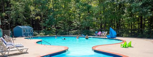 Wide pool view showing the on-site swimming facility and surrounding wooded setting — good facility shot. Source: 'Our Campground' page header image.