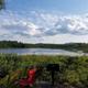 Campsite with lake, chairs, and grill. Kayaker on water.
