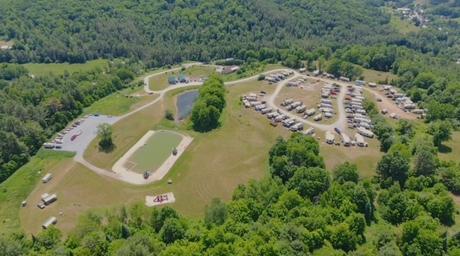 High-angle aerial view showing the pond, parking/entrance and the RV/campsite area — good overall site layout and scale shot from the campground's homepage.