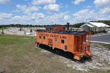Ground-level view of the orange caboose feature with the clubhouse and RV sites visible in the background — distinctive property landmark that reinforces the resort’s name and theme (source: Home page).