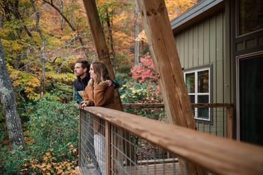 Image of guests on a cabin balcony with fall foliage — conveys guest experience, cabin deck scale and seasonal scenery on the property (gallery/marketing image).