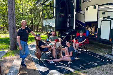 Group relaxing at an RV campsite with a large RV visible — useful photo of the campground’s RV pitches and site setup (trees, spacing, amenities).