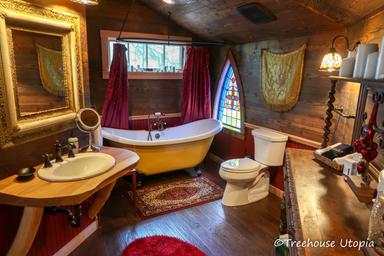Interior bathroom with freestanding tub, stained-glass window and rustic finishes — highlights unique bathroom facilities inside a treehouse (homepage/treehouses imagery).