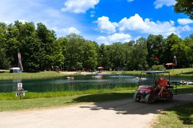 Wide view of the pond/lake with a golf cart in foreground and activity on the water — good overall site view of the campground’s lake and access road. Sourced from the Weekend Camping page on the property site.