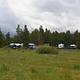 Trucks and trailers in a group campground with a grassy meadow and pines in the background.