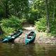 Two green kayaks on shore of river with trees in the background