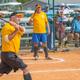 Older man swinging a bat during a softball game, with teammates and spectators watching from behind the fence in Bonita Springs, FL