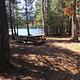 Campsite at Ninemile Campground. There is a picnic table in the shade of several trees and a lake in the background.