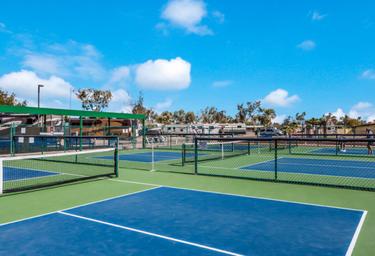 Multiple fenced courts (pickleball/tennis) with RVs visible beyond — highlights on-site recreation facilities featured on the property page.