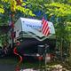Close view of an RV at a wooded campsite with site decorations and hookups visible — useful for illustrating an RV pitch at the campground. Source page context is the property listings for New Hampshire.