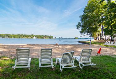 Beach and volleyball area with lounge chairs facing the lake — demonstrates the resort’s lakeside beach recreation spaces. Presented in the resort’s gallery on the property page (page: Lake Gaston RV Camping | Thousand Trails RV Campground, URL provided).