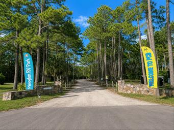 Gravel tree-lined entrance drive with welcome banners — useful exterior shot illustrating campground access and setting.