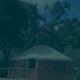 The image shows a yurt with a wooden deck, surrounded by trees under a blue sky with clouds.