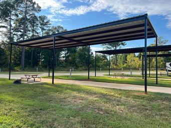 Photo of covered pull-through pads with picnic tables and paved pads beneath metal canopies — highlights site features and shaded RV parking. Source page context shows this as an on-property amenity.