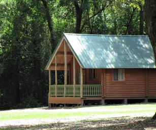 Another high-quality exterior cabin shot (cabin with green roof and trees) that shows setting and scale of lodging; sourced from the accommodations page background.