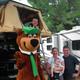 RV campsite area with vehicles and mascot posing — depicts RV parking/pull-through sites and campground setting (homepage gallery image).
