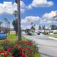 Clear entrance/road view showing the resort sign, landscaped flowerbeds, RV sites, palm trees and flagpole — good overview of the park entrance (homepage image URL).