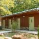 Exterior of a maintained bathhouse/restroom building with multiple doors and landscaped approach — depicts campground facilities. Filename and page placement identify it as the campground bathhouse.