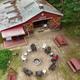 Aerial/overhead view showing the park's central building (barn/rec hall) with a ringed campfire seating area and picnic tables — strong overview of a key guest gathering spot on the property (homepage gallery context).
