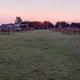Wide sunset view down a grassy central lane showing multiple horse pens/paddocks and RVs/campers at the tree line — good aerial/overview-style shot of the campground layout (image found on the property home page gallery/background).
