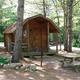 Small cabin on a shaded, wooded campsite with picnic table and grill visible — represents cabin lodging option at this KOA (from waystostay photos on the campground page).