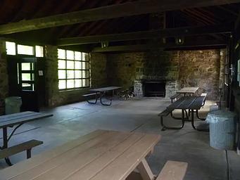 Inside view of the Black River Harbor Pavilion showing the set up of the room with 5 picnic tables, trash can, and fireplace.