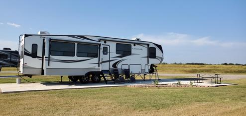 Deluxe pull-through RV site on concrete pad with grassy foreground and open horizon — shows site type and spacing typical at the park (from the rates/amenities pages).