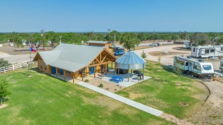 Ground-level view of the clubhouse/building with adjacent RV pad and outdoor seating — highlights facilities and guest areas on the grounds (homepage image showing clubhouse and nearby RV).