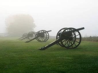 Four civil war cannons along a green foggy field.
